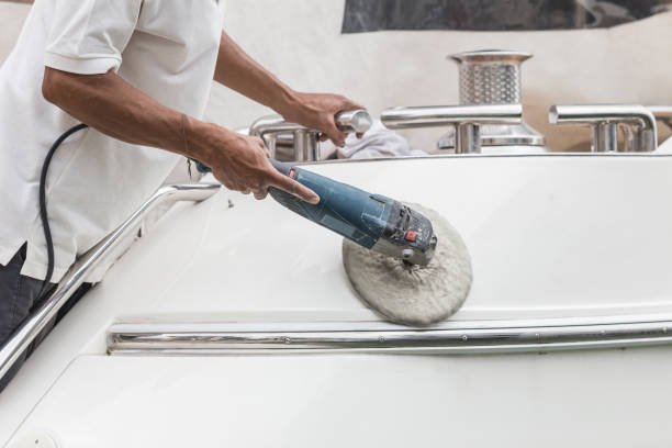 Yacht maintenance. A man polishing side of the white boat by grinder machine in the marina